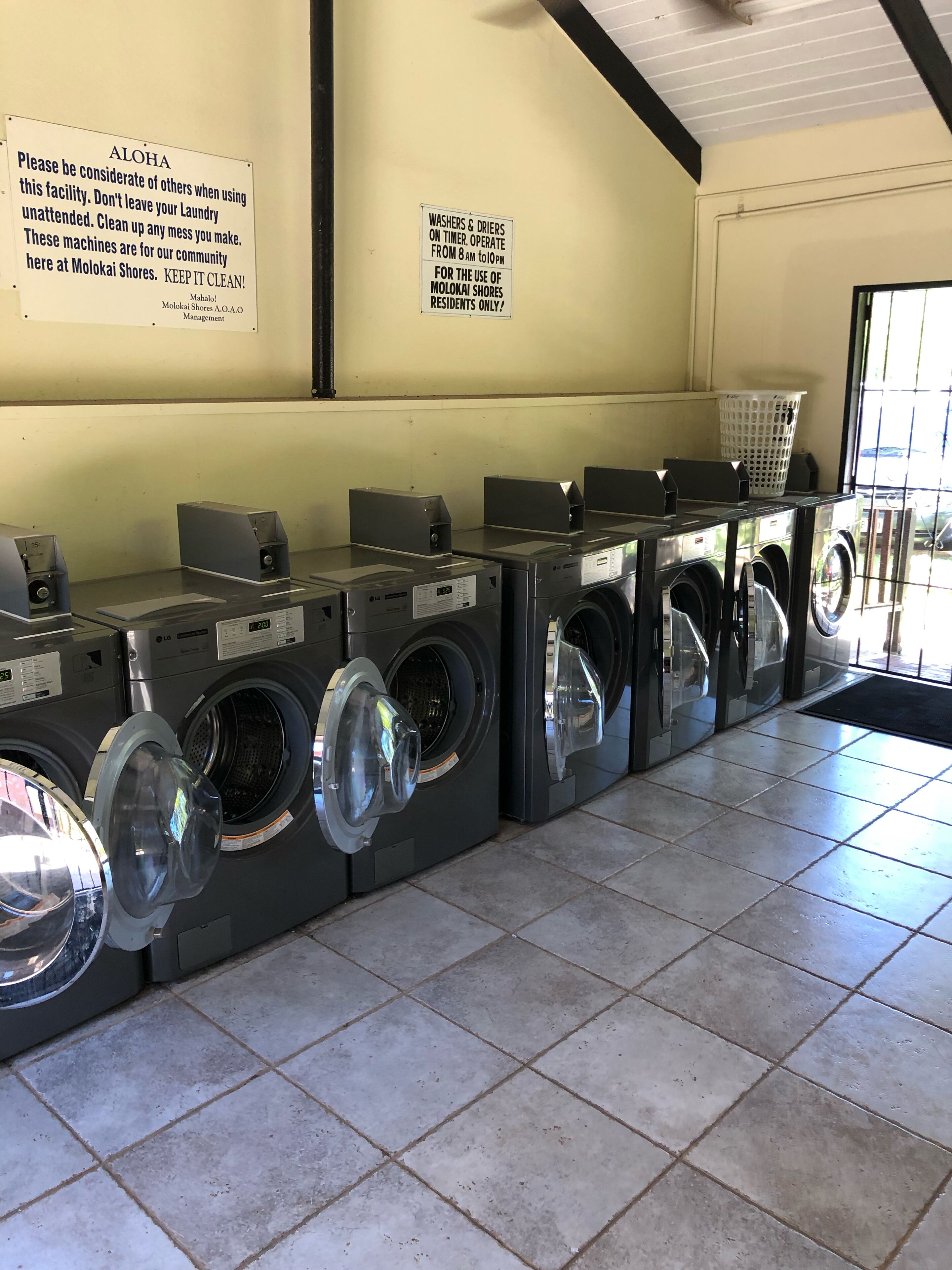 A laundry facility with multiple washing machines and dryers, signs indicating usage rules, and a tiled floor.