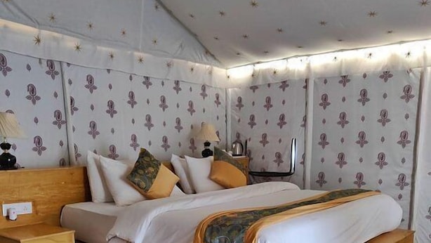A room with a wooden bed, patterned wallpaper, and a colorful rug. - Country side resort Jaisalmer (Jaisalmer)