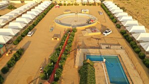 Vista aérea de un resort en el desierto con varias tiendas blancas dispuestas en filas, una piscina central y un paseo circular.