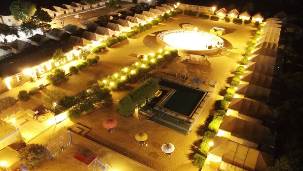 Vista aérea de un espacio al aire libre bien iluminado con tiendas de campaña, una piscina y un área circular para reuniones.