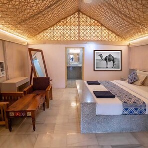 Un dormitorio con cama, un banco, un espejo y una imagen de un camello en la pared.