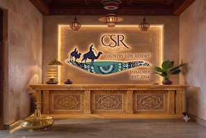 Una recepción con un diseño de madera tallada, un cartel que dice 'CSR Country Side Resort Jaisalmer EST. 2014' y una lámpara decorativa.