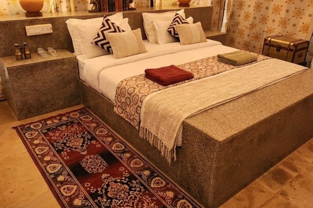 Quarto com cama, mesas de cabeceira, luminárias e um tapete estampado.