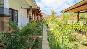 Un chemin menant à un bâtiment doté d’un porche abrité et d’un jardin planté de plantes et de fleurs tropicales.