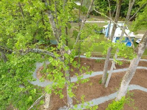 Stroll through the serene outdoor space surrounded by lush greenery and mature trees, along a winding pathway bordered by neatly arranged mulch.