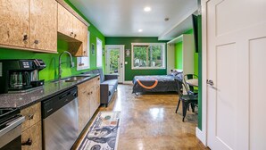 A compact kitchen with a coffee maker, a sink, and wooden cabinets. There is a bed with a colorful bedspread in the adjacent room. - Bike Studio Apartment Near Everything! (Brevard)