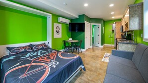 A modern bedroom with a bed, a small table, and a sofa. There is a kitchen area with a sink and a countertop. - Bike Studio Apartment Near Everything! (Brevard)