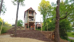A two-story building with a balcony, surrounded by trees and a gravel path. - Bike Studio Apartment Near Everything! (Brevard)