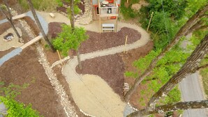 A landscaped garden area with a winding path, trees, and a small building with a red door. - Bike Studio Apartment Near Everything! (Brevard)