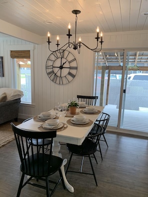 A dining area with a large table set for four, surrounded by black chairs, a chandelier, and a large wall clock.