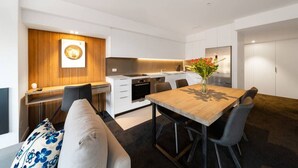 Eine moderne Küche mit weißen Schränken, einer Wand in Holzoptik und einem Essbereich mit Holztisch und -stühlen.
