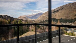 Ein Balkon mit Blick auf eine gebirgige Landschaft, darunter ein verschneiter Berggipfel und ein Tal mit Bäumen.