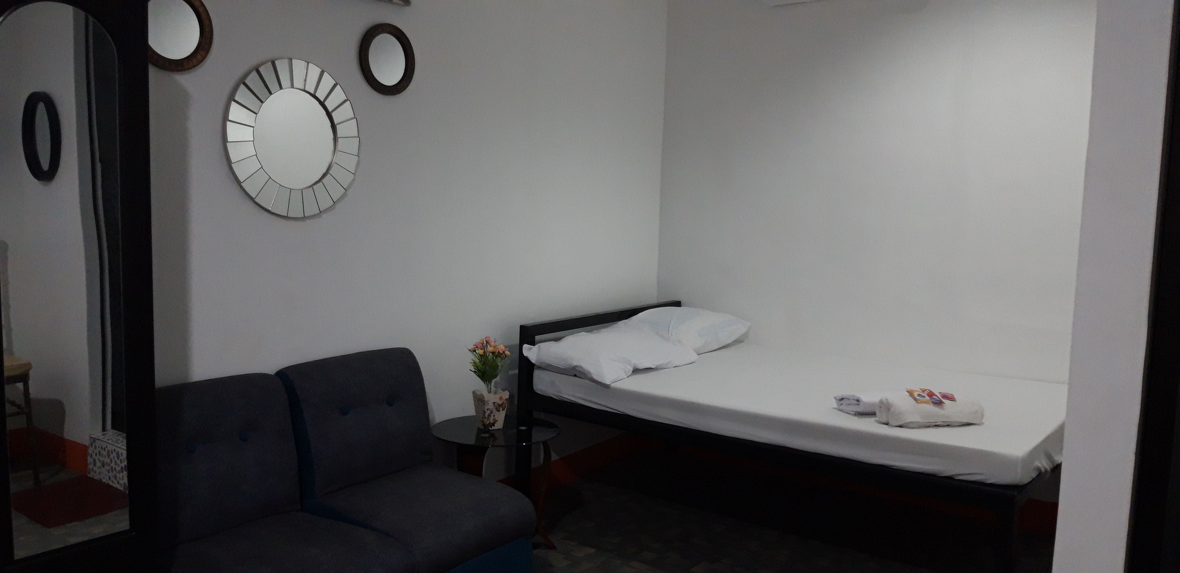 Een kleine, eenvoudige kamer met een bed, een bank en een spiegel aan de muur.