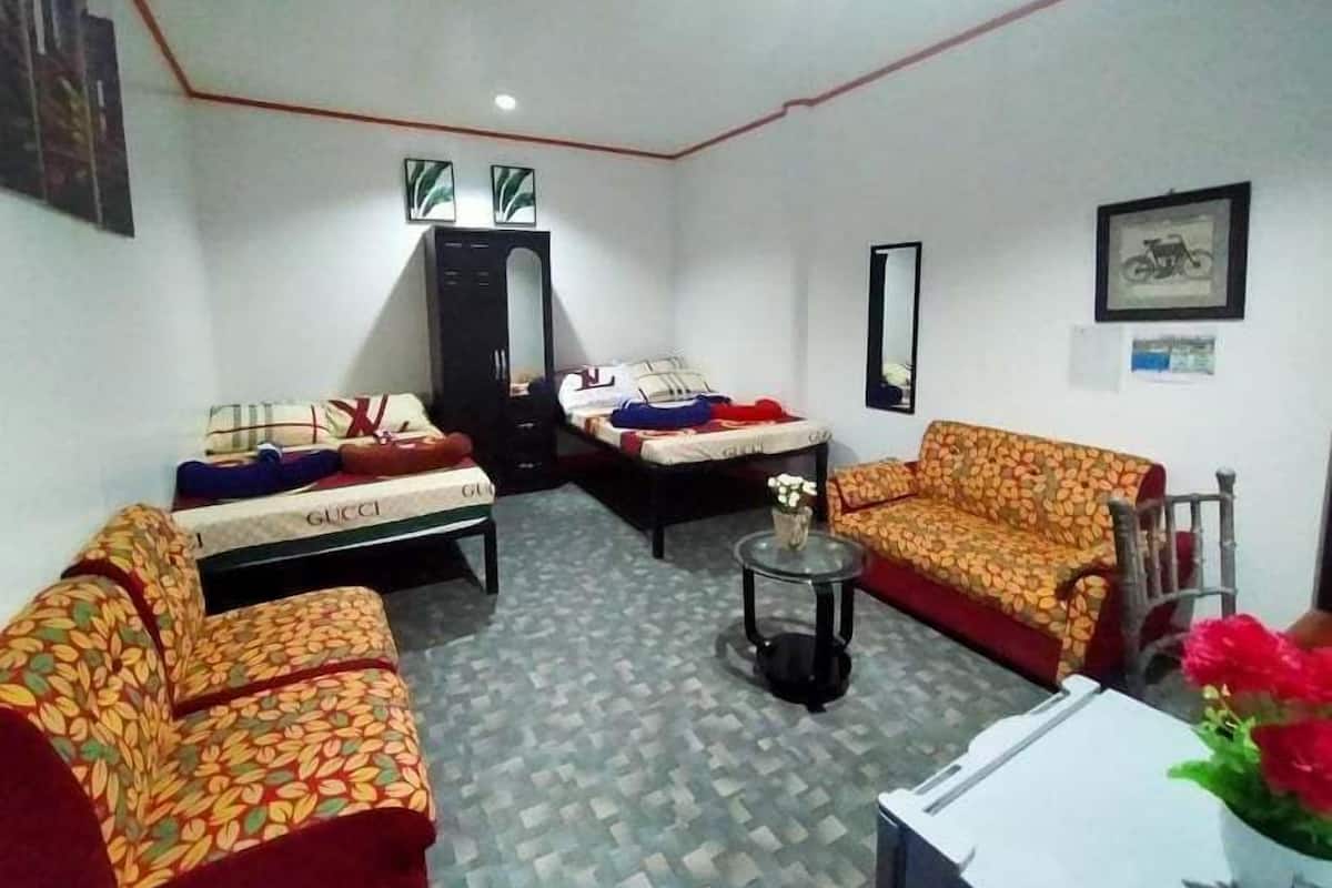 A room with two beds, a sofa, a small table, and a mirror on the wall.