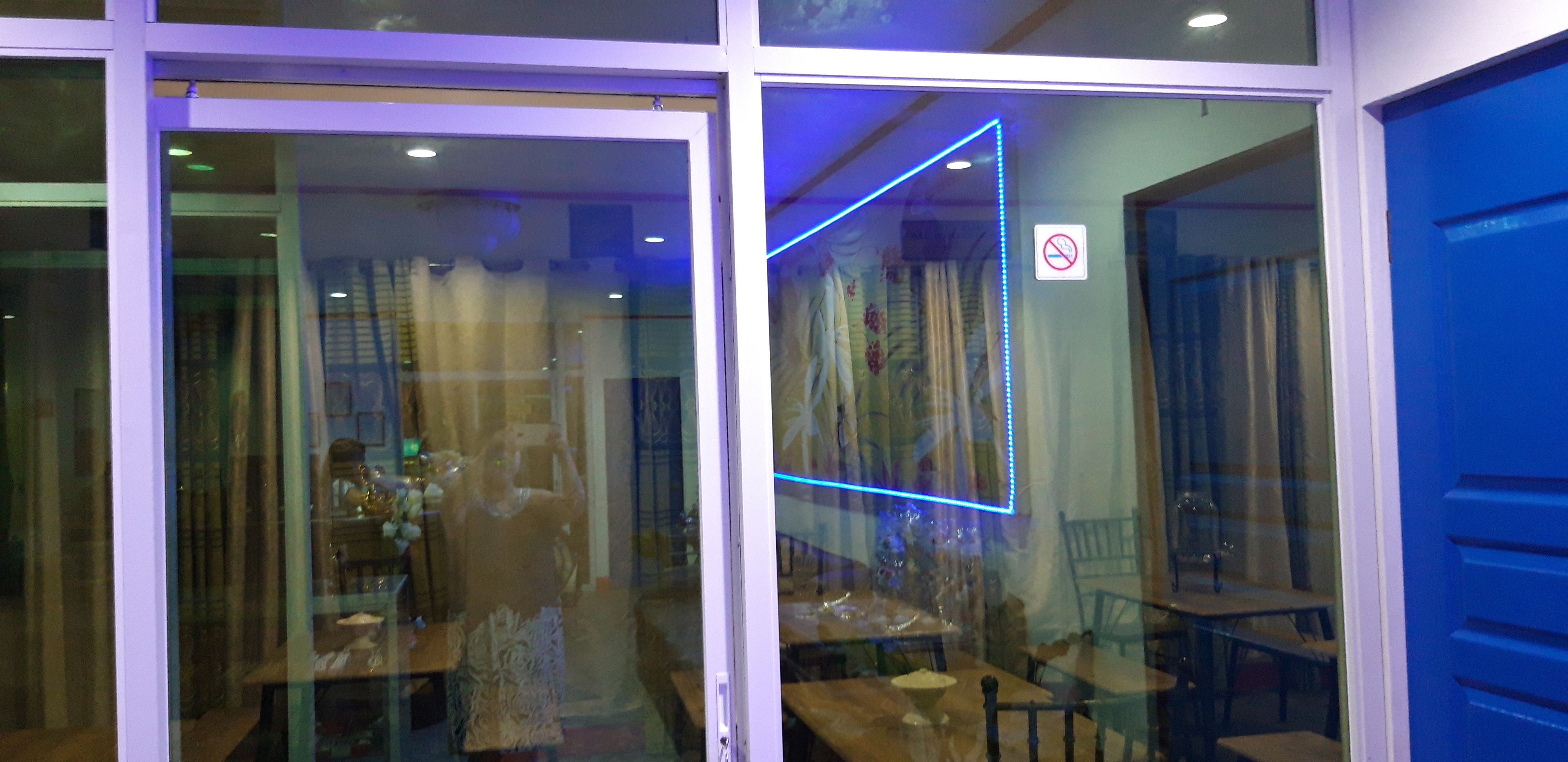 A restaurant interior with tables and chairs, a blue neon light, and a no smoking sign.