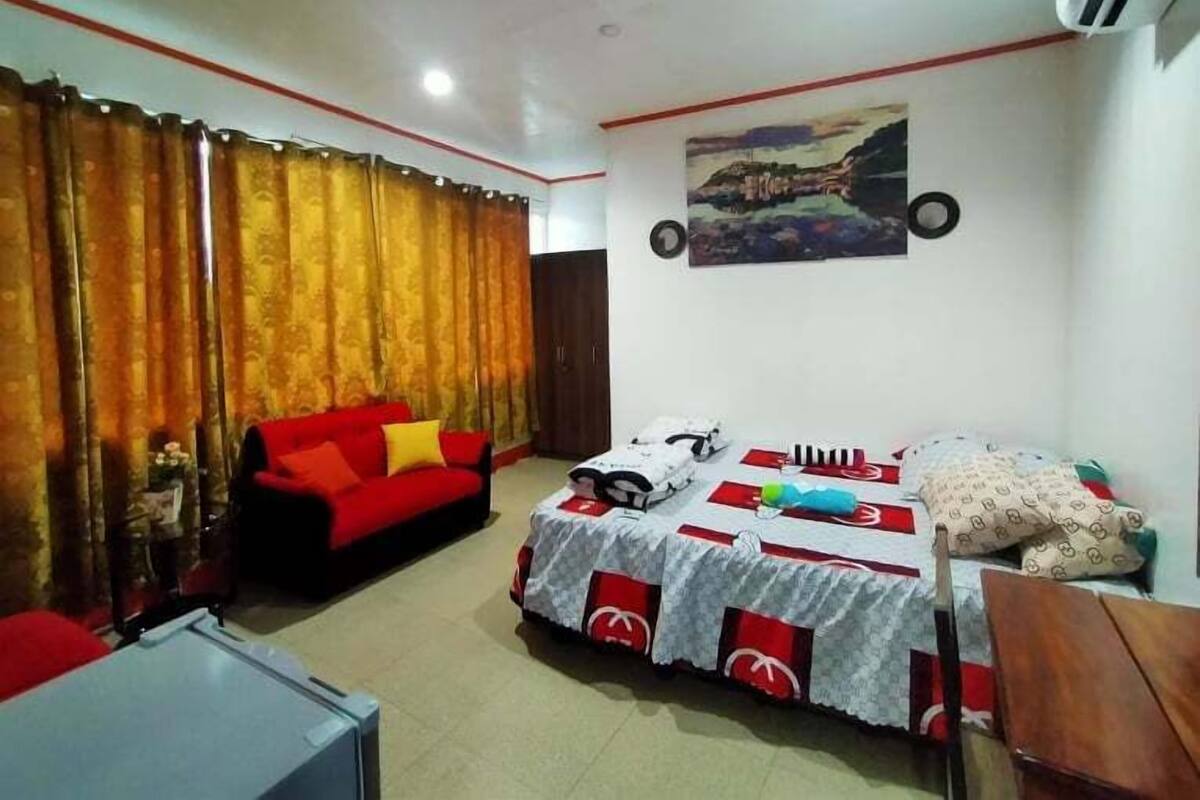 A room with a bed, a red sofa, a table, and a painting on the wall.