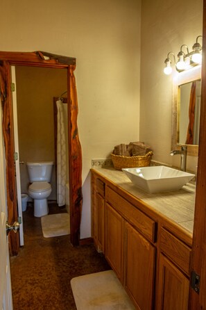 Ein Badezimmer mit Holzschränken, einem weißen Waschbecken, einem Spiegel mit Beleuchtung, einer Toilette und einer Duschvorhang.