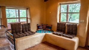 A cozy room with two cushioned seating areas against the walls, a wooden chair, and a colorful woven rug.