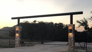 A gated entrance with a metal gate and stone pillars, leading to a dirt path.