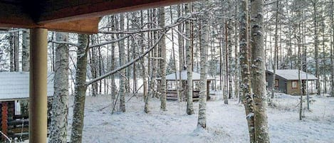 A wooden cabin with a snow-covered deck and a view of a forested area.
