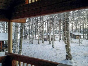 Una cabaña de madera con una terraza cubierta de nieve y vistas a un área boscosa.