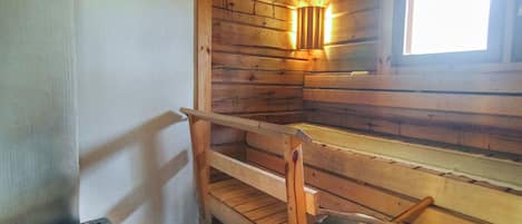 A cabin with wooden walls, a window, a metal bucket, and a small container of rocks.