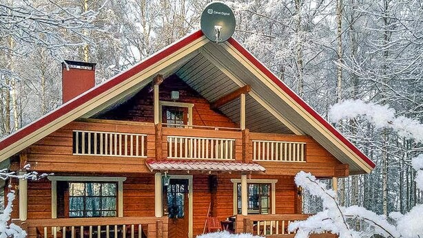Una cabaña de madera de dos pisos con un balcón, rodeada de árboles cubiertos de nieve.