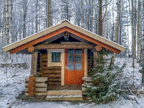 Hirsihökkelissä on puuovi ja -ikkunat, ja se on lumipeitteisten puiden ympäröimänä.