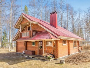 Una cabaña de madera de dos pisos con techo rojo, un balcón y una chimenea.