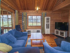 A cozy cabin interior with a sofa, a table, a cabinet, and a television.