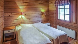 Una habitación de cabaña de madera con cama, mesitas de noche y ventana con vista a árboles.