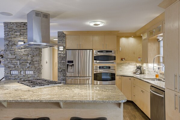 A modern kitchen with a granite countertop, stainless steel appliances, wooden cabinets, and a stone accent wall.