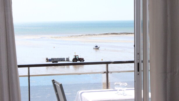 Vista desde un balcón sobre una playa, con un tractor y un bote en el agua.