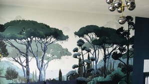 Una sala de estar con un sofá azul oscuro, dos mesas auxiliares redondas, un tapete blanco y una zona de comedor con sillas color turquesa.