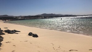 A beach with clear water, a sandy shore, and distant mountains.