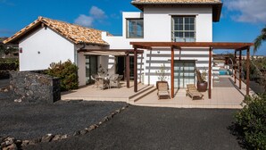 A modern two-story house with a tiled roof, a covered patio with outdoor furniture, and a swimming pool.
