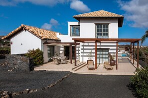 A modern two-story house with a tiled roof, a covered patio with outdoor furniture, and a swimming pool. - Beautiful Villa with Pool, Pool Bar, Terraces & Wi-Fi (Lajares)