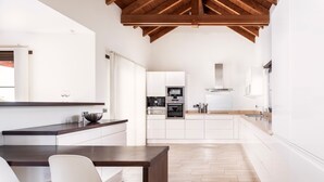 A modern kitchen with white cabinetry, a wooden ceiling, and a dining area with a dark wood table and white chairs.