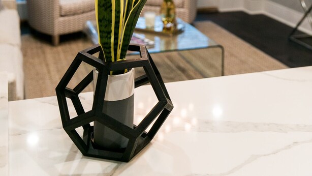 Un salon doté d’une grande fenêtre, d’une plante dans un vase aux motifs géométriques et d’un lustre.