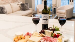 Un plan de travail en marbre agrémenté d’une planche à charcuterie, de verres à vin et d’une bouteille de vin Chloe, dans un salon moderne avec un mur en briques et de grandes fenêtres.