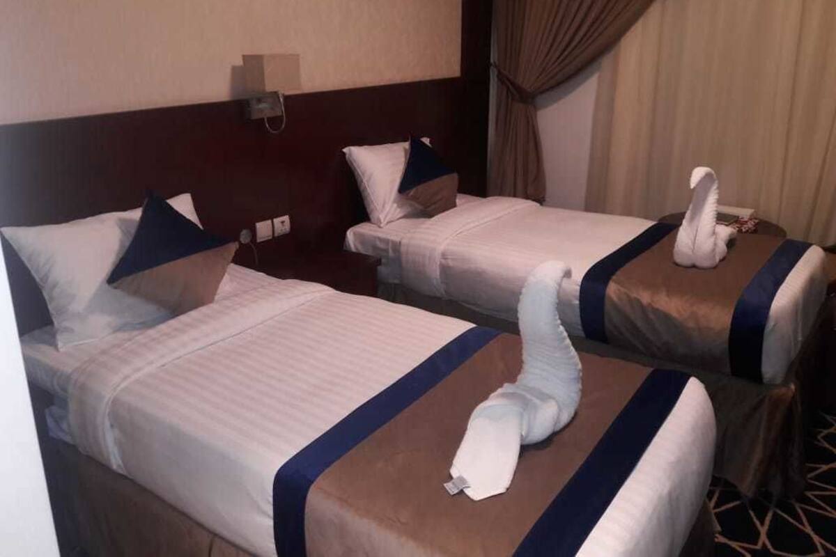 Deux lits d’hôtel avec des serviettes pliées en forme de cygnes, une tête de lit et un rideau.