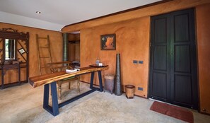Ein Zimmer mit einem Holztisch, einem gerahmten Bild an der Wand, einer schwarzen Tür und einer kleinen Mülltonne.