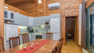 A wooden cabin interior with a kitchen, dining area, and a glass door leading outside.