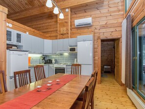 A wooden cabin interior with a kitchen, dining area, and a glass door leading outside. - Villa tilia by Interhome (Pertunmaa)