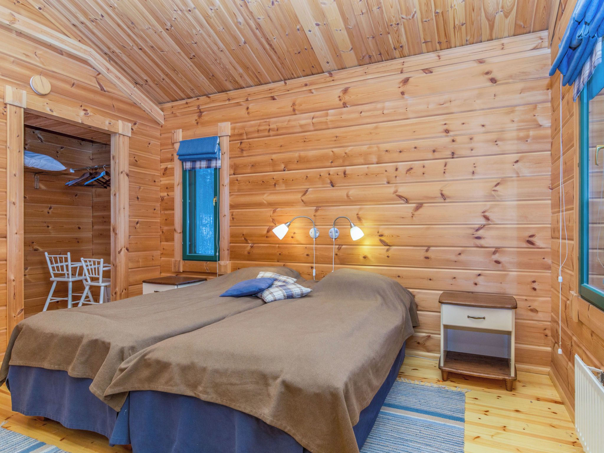 Ein Schlafzimmer einer Holzhütte mit zwei Betten, einem kleinen Tisch, einem Stuhl und einem Fenster mit Vorhängen.