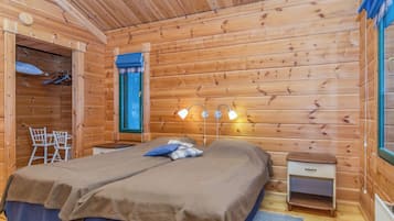 Ein Schlafzimmer einer Holzhütte mit zwei Betten, einem kleinen Tisch, einem Stuhl und einem Fenster mit Vorhängen.