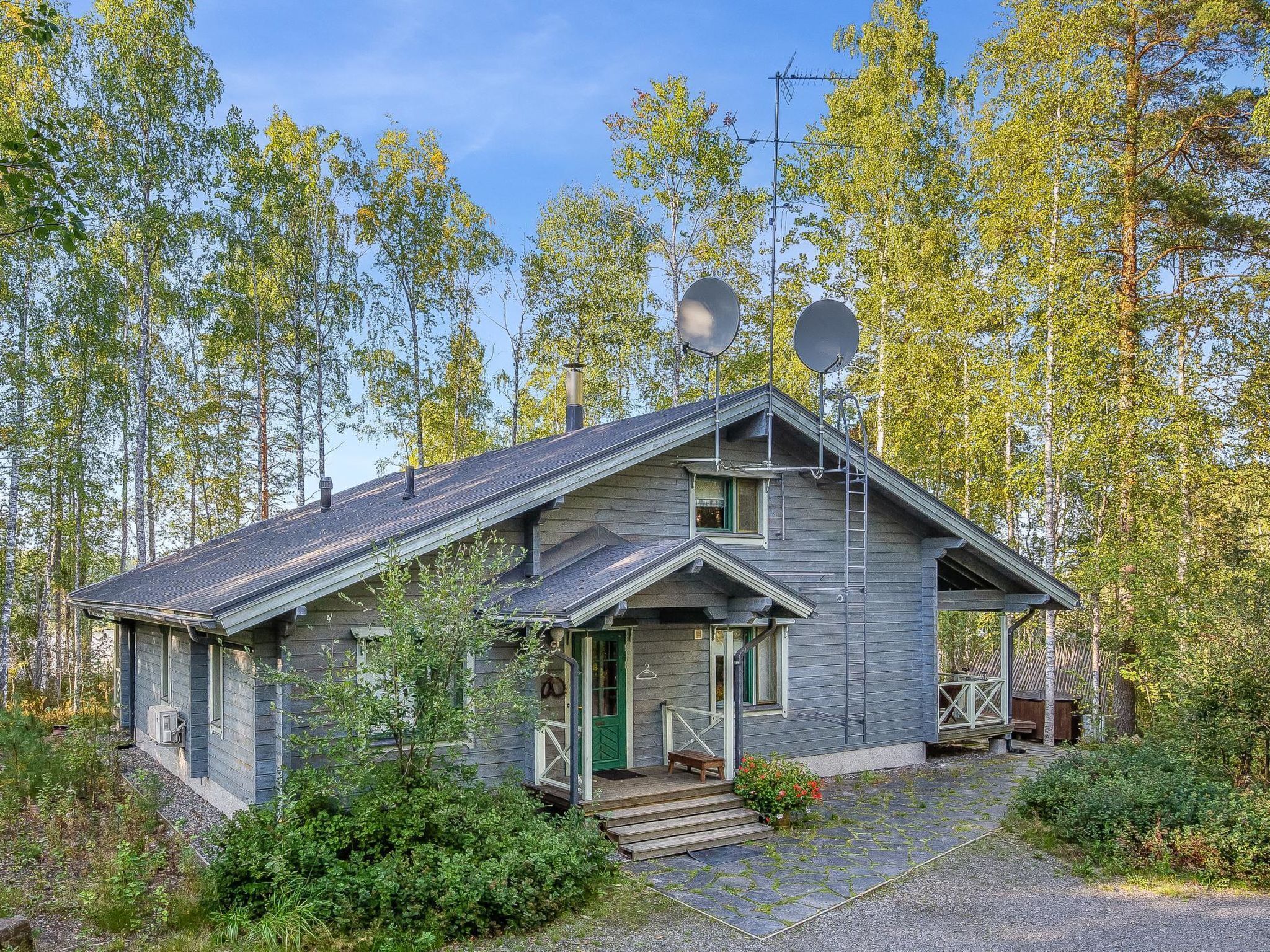 Pieni, kaksikerroksinen mökki, jossa on kalteva katto, ja sen ympärillä on tiheää metsää.