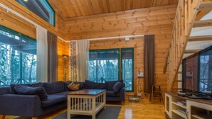 A cozy cabin interior with a wooden floor, a sofa, a coffee table, and a TV on a wooden stand.