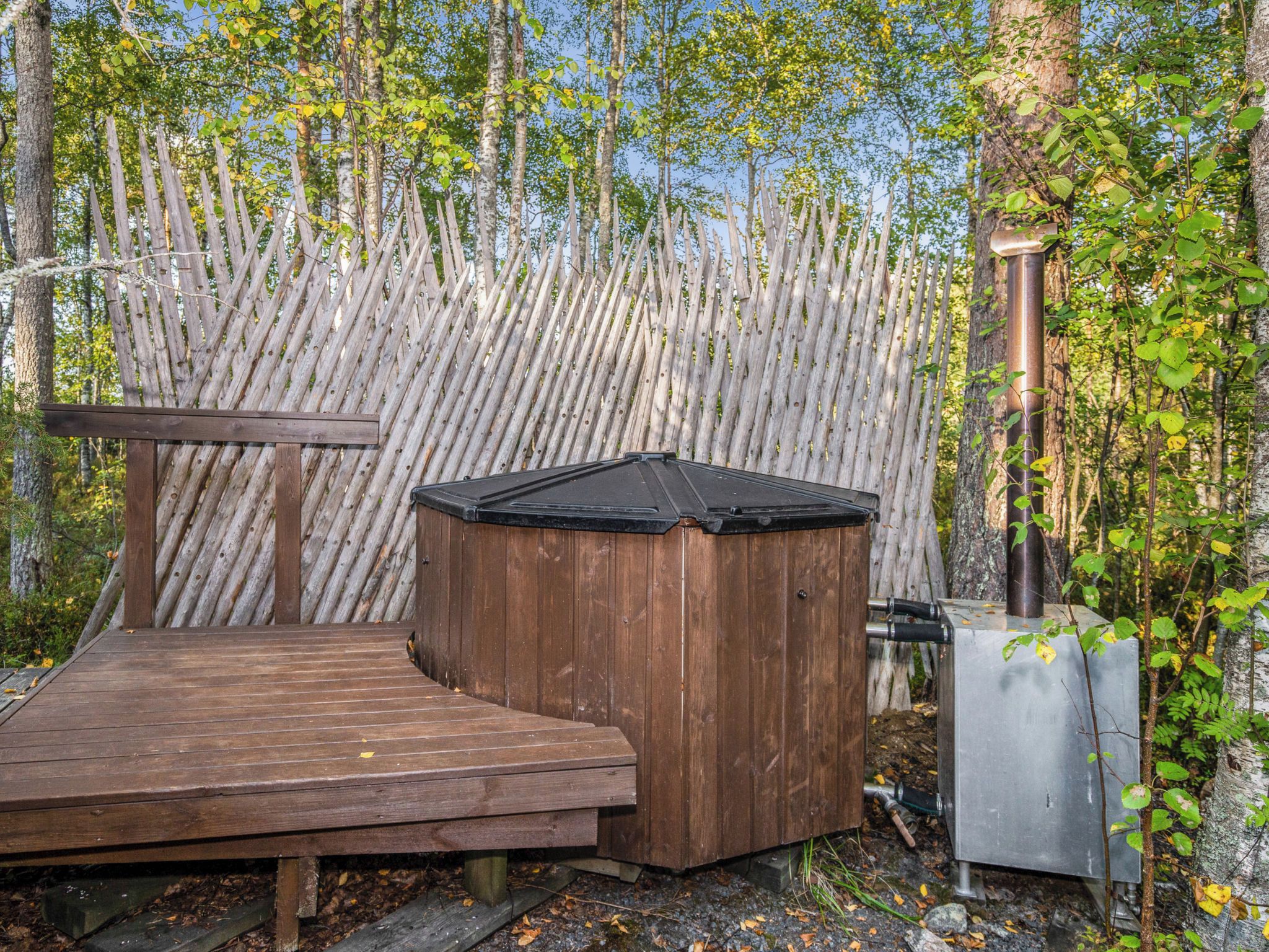 Eine Holzterrasse mit Whirlpool und Sauna in bewaldeter Landschaft.