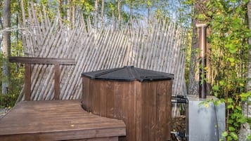 Eine Holzterrasse mit Whirlpool und Sauna in bewaldeter Landschaft.